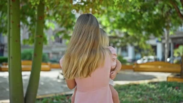 Madre segura, brazos envueltos alrededor de su hija, sonriendo alegremente de pie en el parque iluminado por el sol, irradiando positividad y felicidad - Imágenes, Vídeo