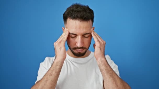 Junger arabischer Mann leidet unter Kopfschmerzen vor isoliertem blauen Hintergrund - Filmmaterial, Video