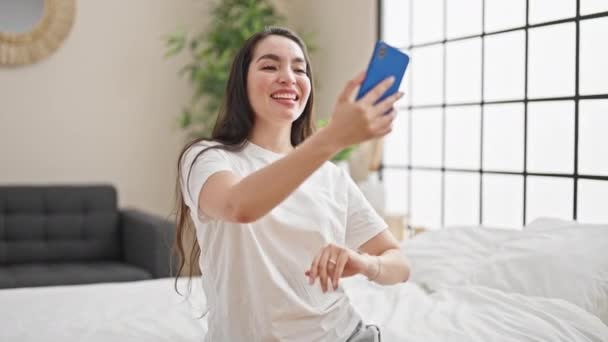 Giovane bella donna ispanica che fa videochiamata seduta sul letto in camera da letto - Filmati, video