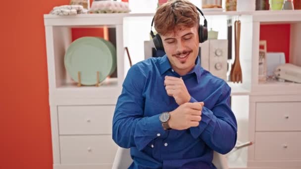 Jonge Spaanse man die naar muziek luistert zittend op tafel dansend in de eetzaal - Video