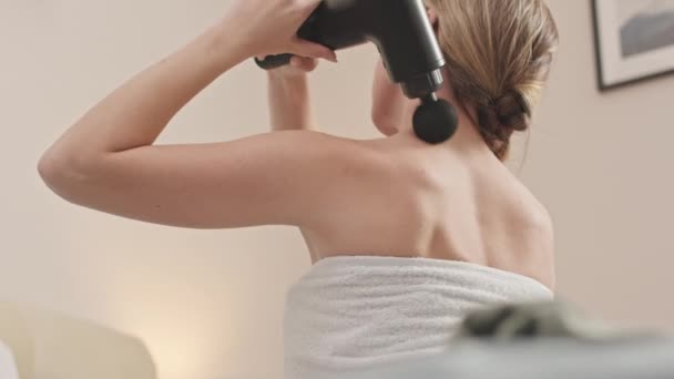 Joven hermosa mujer caucásica usando pistola de masaje en su espalda después de la ducha de la mañana - Imágenes, Vídeo