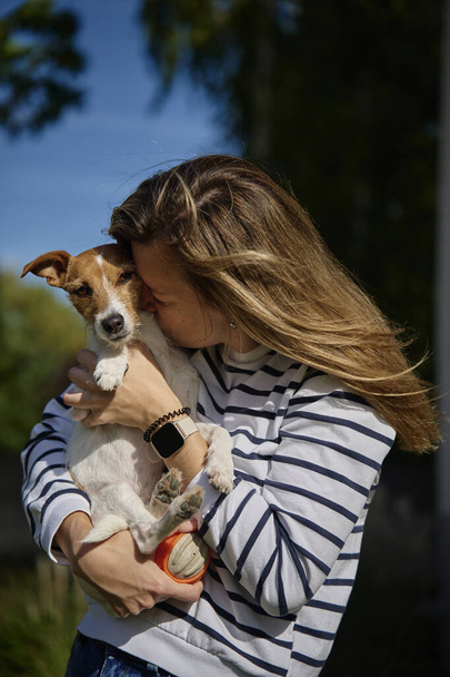 La mujer sostiene a su perro en las manos y se abraza con él. Feliz dueño femenino abrazando y besando amigo lindo. Cuidado de mascotas - Foto, Imagen