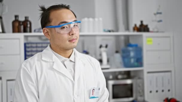 Magabiztos, fiatal kínai tudós élvezi munkáját, boldogan mosolyog, miközben a nyüzsgő laborban áll, az orvosi kutatás és technológia izgalmai közepette.. - Felvétel, videó