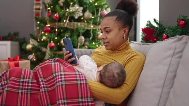 Äiti ja poika juhlivat joulua älypuhelimella imettäessään vauvaa kotona - Materiaali, video