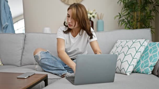 Nuori nainen puhuu älypuhelimella kannettavan tietokoneen avulla kotona - Materiaali, video