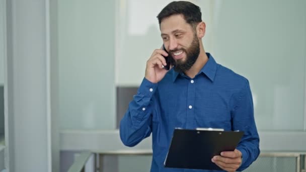 Mladý hispánec muž obchodní pracovník čtení dokumentu mluvit na smartphone v kanceláři - Záběry, video