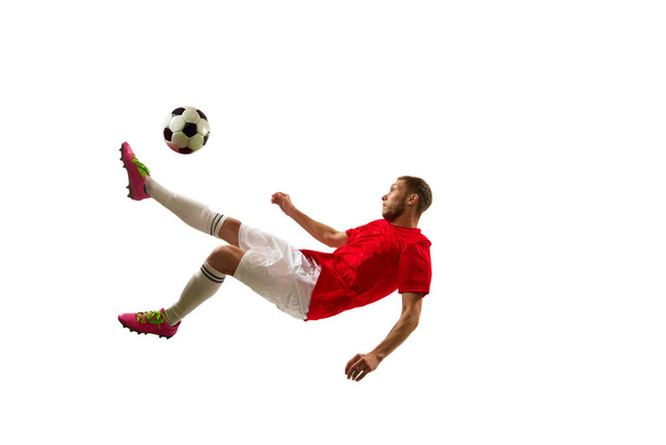 Jonge voetballer ziet er vol vertrouwen in sportschoeisel en laarzen schoppen bal voor doel in sprong tegen een witte achtergrond. Voetbalschool. Begrip spel, sport, recreatie, actieve levensstijl. - Foto, afbeelding