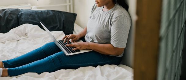 ベッドの上でラップトップを使用してアフリカ系アメリカ人の若い女性-技術と通信とソーシャルネットワーク - 写真・画像