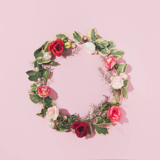 Rosen und Perlen mit Kranz aus frischen Blättern arrangiert, romantischer Blumenrahmen mit kreativem Kopierraum, pastellrosa Hintergrund.  - Foto, Bild