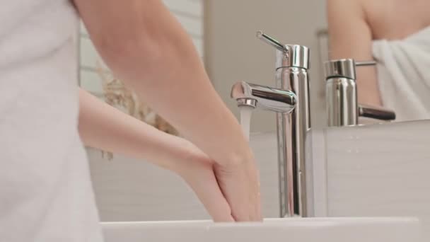 浴室のシンクで彼女の手を洗う白いタオルを身に着けている認識できない若い女性のクロップバックビューショット - 映像、動画