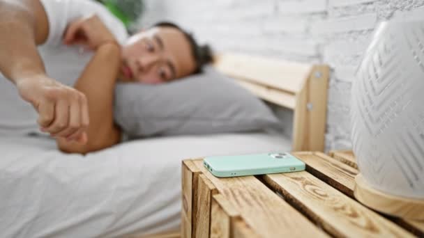Joven hombre chino buscando tiempo en el teléfono inteligente durmiendo en el dormitorio - Metraje, vídeo