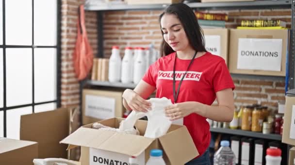 Young beautiful hispanic woman volunteer smiling confident packing cardboard box at charity center - Footage, Video
