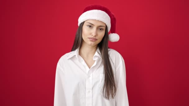 Joven mujer hispana hermosa usando sombrero de Navidad sufriendo de dolor de cabeza sobre fondo rojo aislado - Imágenes, Vídeo