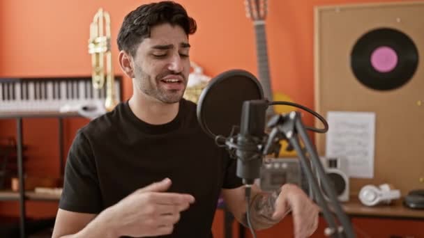 Junger hispanischer Musiker lächelt selbstbewusst und singt Song im Musikstudio - Filmmaterial, Video
