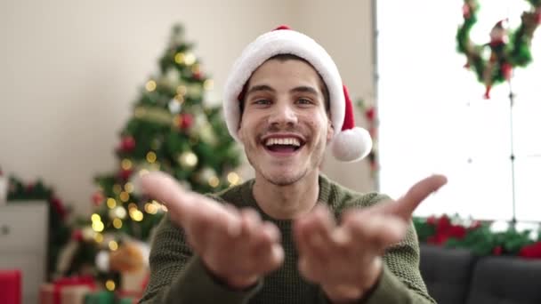 Junger hispanischer Mann sitzt auf Sofa am Weihnachtsbaum und küsst sich zu Hause - Filmmaterial, Video