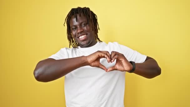 Αφροαμερικάνος χαμογελαστός με αυτοπεποίθηση κάνει χειρονομία καρδιάς με τα χέρια πάνω από απομονωμένο κίτρινο φόντο - Πλάνα, βίντεο