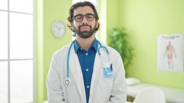 Jonge Spaanse man dokter glimlachend vol vertrouwen staand in de kliniek - Video