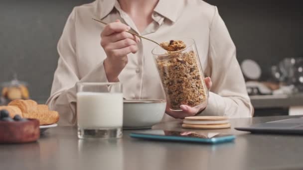 Rajattu laukaus tunnistamaton nainen kultalusikalla ja lisäämällä terveellistä mysliä kulhoon maitoa, ottaa terveellisen aamiaisen kotona - Materiaali, video