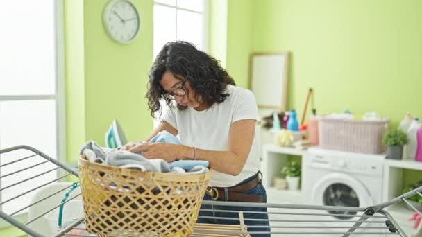 Middle age hispanic woman leaning of basket with clothes stressed at laundry room - Footage, Video