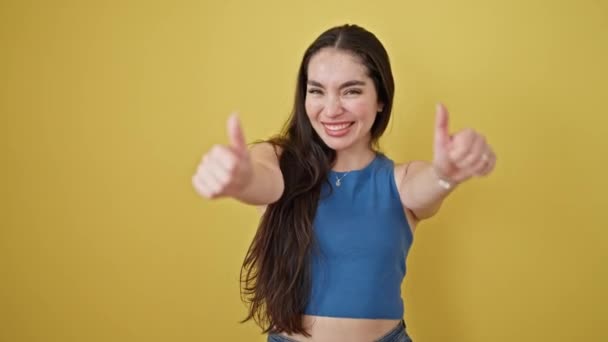 Young beautiful hispanic woman smiling with thumbs up over isolated yellow background - 映像、動画