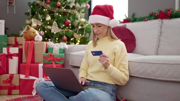Mujer rubia joven de compras con ordenador portátil y tarjeta de crédito sentado en el suelo por el árbol de Navidad en casa - Metraje, vídeo