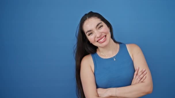 Fiatal gyönyörű spanyol nő áll a karját keresztbe tett gesztussal mond igen kézzel át elszigetelt kék háttér - Felvétel, videó