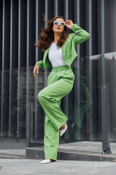 Μοντέρνο κομψό αυτοπεποίθηση γυναίκα φορώντας μοντέρνα ροζ γυαλιά ηλίου, μεταξωτή μαντίλα, σακάκι κοστούμι, με πράσινη τσάντα, ποζάρουν στο δρόμο της ευρωπαϊκής πόλης. Πορτραίτο μόδας. Αντιγραφή, κενό χώρο για κείμενο - Φωτογραφία, εικόνα