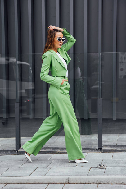 Μοντέρνο κομψό αυτοπεποίθηση γυναίκα φορώντας μοντέρνα ροζ γυαλιά ηλίου, μεταξωτή μαντίλα, σακάκι κοστούμι, με πράσινη τσάντα, ποζάρουν στο δρόμο της ευρωπαϊκής πόλης. Πορτραίτο μόδας. Αντιγραφή, κενό χώρο για κείμενο - Φωτογραφία, εικόνα