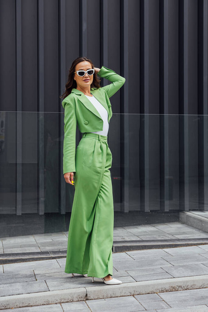 Módní elegantní sebevědomá žena v módních růžových slunečních brýlích, hedvábném šátku, sako, se zelenou taškou, pózující na ulici evropského města. Venkovní módní portrét. Kopírovat, prázdné místo pro text - Fotografie, Obrázek