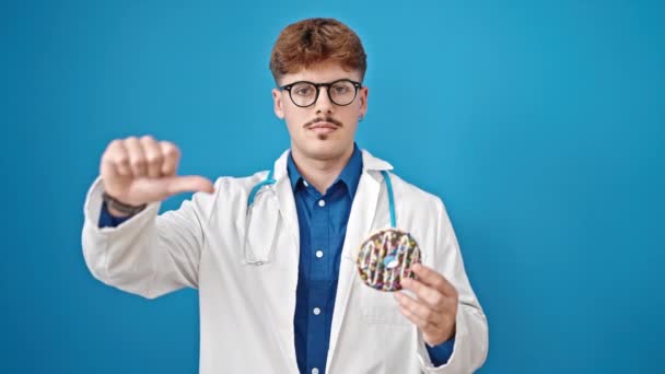 Giovane ispanico uomo medico holding ciambella fare pollice giù gesto su isolato blu sfondo - Filmati, video