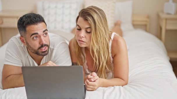 Άνδρας και γυναίκα ζευγάρι ξαπλωμένοι στο κρεβάτι μαζί χρησιμοποιώντας το φορητό υπολογιστή κοιτάζοντας γύρω στο υπνοδωμάτιο - Πλάνα, βίντεο