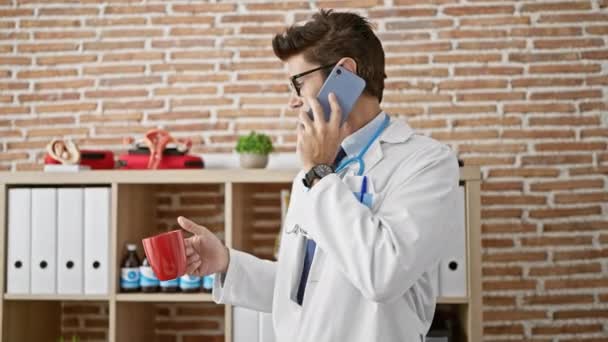 Jeune homme hispanique médecin parlant sur smartphone boire du café à la clinique - Séquence, vidéo