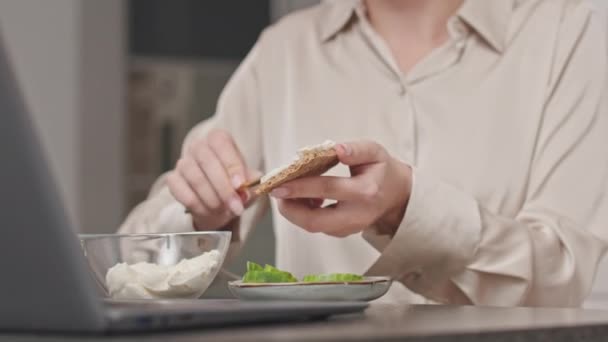 Schnappschuss einer unkenntlichen Frau, die beim Frühstück zu Hause am Wochenende Bio-Frischkäse über Knäckebrot streut und Gurkenscheiben darauf legt - Filmmaterial, Video