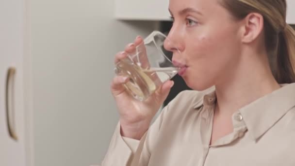 Γείρε από νεαρή όμορφη Καυκάσια γυναίκα κύλιση στο smartphone, ενώ πίνοντας φρέσκο νερό λεμόνι στέκεται στη σύγχρονη κουζίνα - Πλάνα, βίντεο