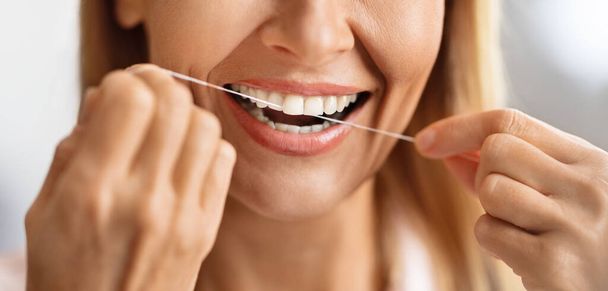 Στοματική φροντίδα. Κοντινό πλάνο της χαμογελώντας ώριμη γυναίκα χρησιμοποιώντας οδοντικό νήμα, αγνώριστη μεσήλικη γυναίκα καθαρισμού τέλεια λευκά δόντια, ευτυχισμένη κυρία κάνοντας καθημερινή ρουτίνα υγιεινής στο σπίτι, περικοπεί εικόνα - Φωτογραφία, εικόνα