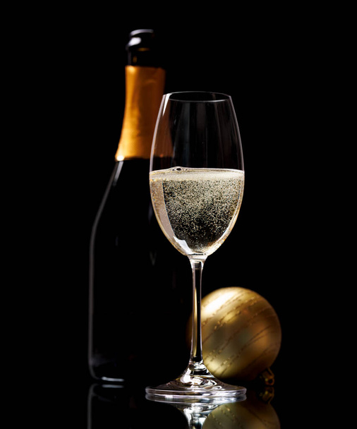 Бокал шампанского, безделушка и бутылка на черном фоне - Фото, изображение