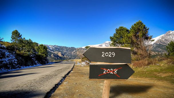 An image with a signpost pointing in two different directions in German. One direction points to 2029 the other points to 2028. - Photo, Image