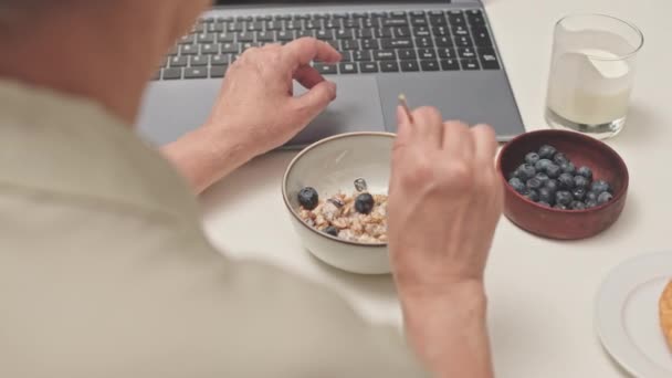 Olkapään yli tunnistamaton nainen sekoittamalla mysliä luonnon jogurtti ja marjoja, ottaa terveellisen aamiaisen kotona - Materiaali, video