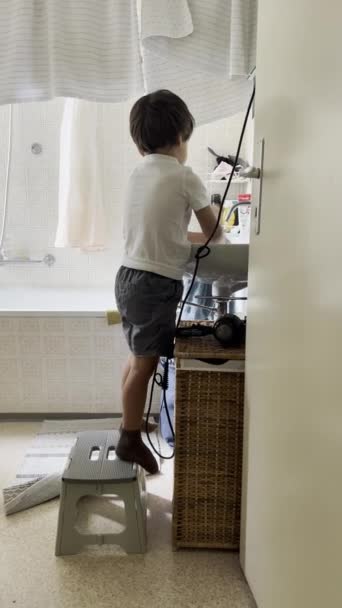 Katsella kuin pieni, omavarainen nuori poika pesee kätensä itsenäisesti korkealla pesuallas, taitavasti käyttäen askel ulosteesta apua - Materiaali, video