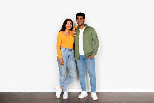 Iloinen nuori intialainen puolisot pukeutunut moderni rento vaatteita, luottavaisesti seisoo yhdessä vastaan puhdas valkoinen tausta, tihkuu lämpöä ja toveruus - Valokuva, kuva
