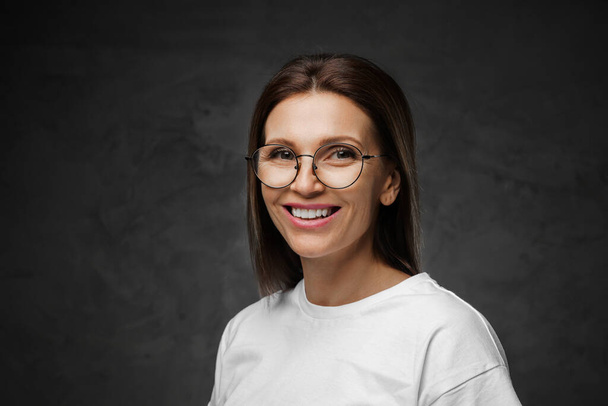 Delighted female in spectacles and white tee beams brightly with a moody backdrop - Fotoğraf, Görsel