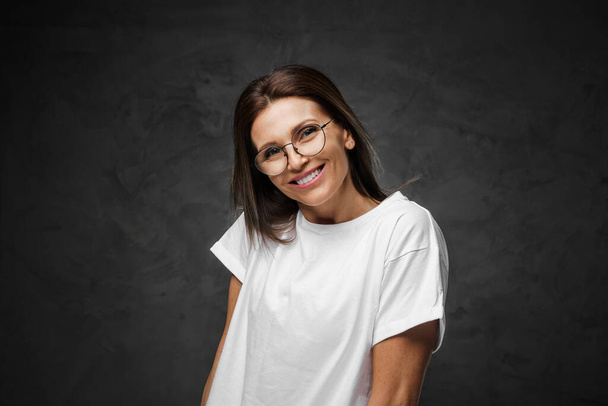 Gözlüklü keyifli bir kadın ve hüzünlü bir arka planla ışıl ışıl beyaz tişörtler. - Fotoğraf, Görsel