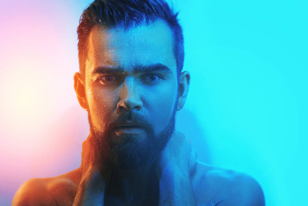 Portrait of handsome young man with wet face in blue and orange light - Foto, Bild