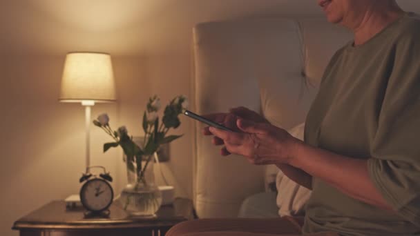Vanhempi aasialainen nainen viimeistely selailu älypuhelimeen, sammuta valo ja menossa nukkumaan yöllä - Materiaali, video