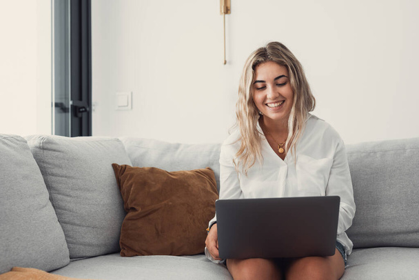 Portrét jedné mladé atraktivní blondýny pomocí notebooku PC na gauči relaxaci surfování na internetu doma. Práce on-line koncept životního stylu - Fotografie, Obrázek