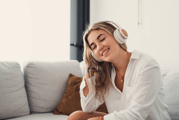 Pokojowa dziewczyna w nowoczesnych bezprzewodowych słuchawkach siedzieć zrelaksować się na wygodnej kanapie słuchając muzyki, szczęśliwy spokojny młoda kobieta w słuchawki odpocząć na przytulnej kanapie, cieszyć się dobrą jakość dźwięku, bezstresowe pojęcie - Zdjęcie, obraz