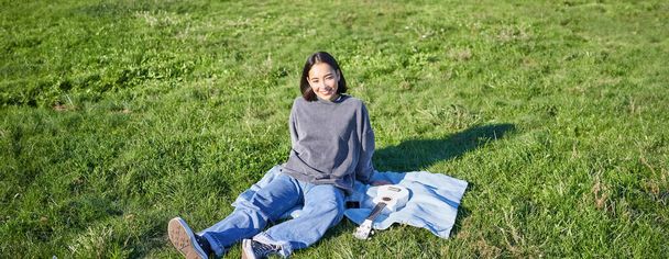 Młoda Azjatka ciesząca się słonecznym dniem na świeżym powietrzu. szczęśliwy student mając piknik na trawie w parku, gra ukulele. - Zdjęcie, obraz