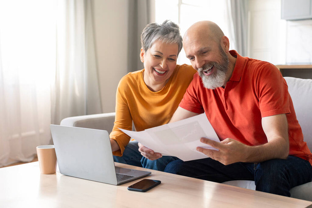 Glückliche ältere Ehepartner, die zu Hause Finanzunterlagen prüfen und das Familienbudget berechnen, fröhliches älteres Paar, das im Wohnzimmer am Tisch sitzt, Kreditpapiere liest oder monatliche Ausgaben zählt - Foto, Bild
