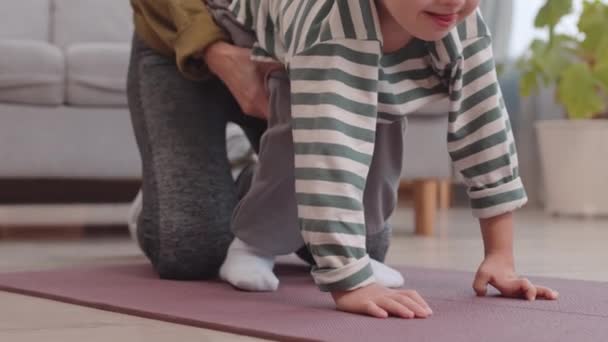 Kaukaski chłopiec z zespołem Downa robi ćwiczenia fizyczne na macie podczas rekreacji z mamą w przytulnym domu - Materiał filmowy, wideo