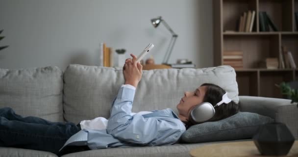 Poika makaa mukavasti sohvalla, käyttää kuulokkeita ja syventynyt puhelimeen. Hänen järkähtämätön keskittymisensä on käsin kosketeltavaa, kun hän sukeltaa digitaaliseen maailmaan, jota ympäristö ei häiritse.. - Materiaali, video
